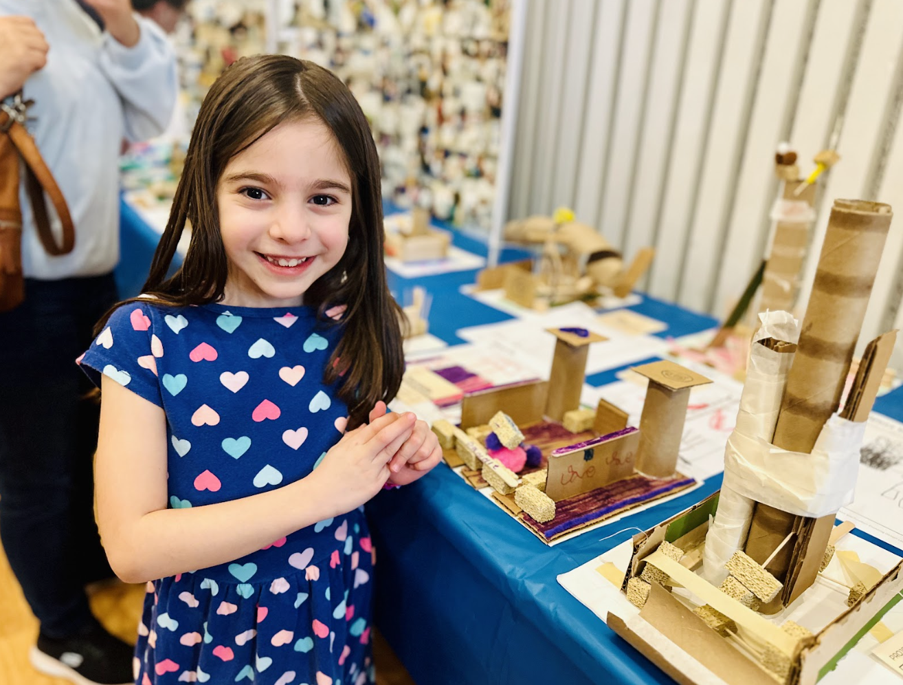 a child stands in front of their science project at a classroom exhibition.