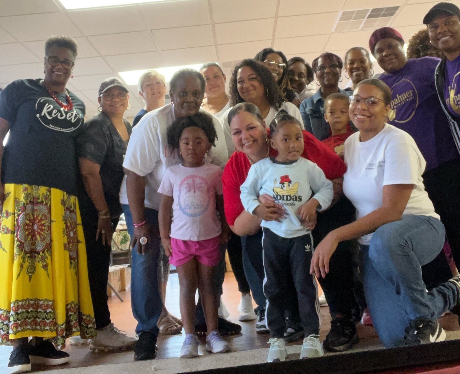 A group of volunteers posing with children in a recreation room.