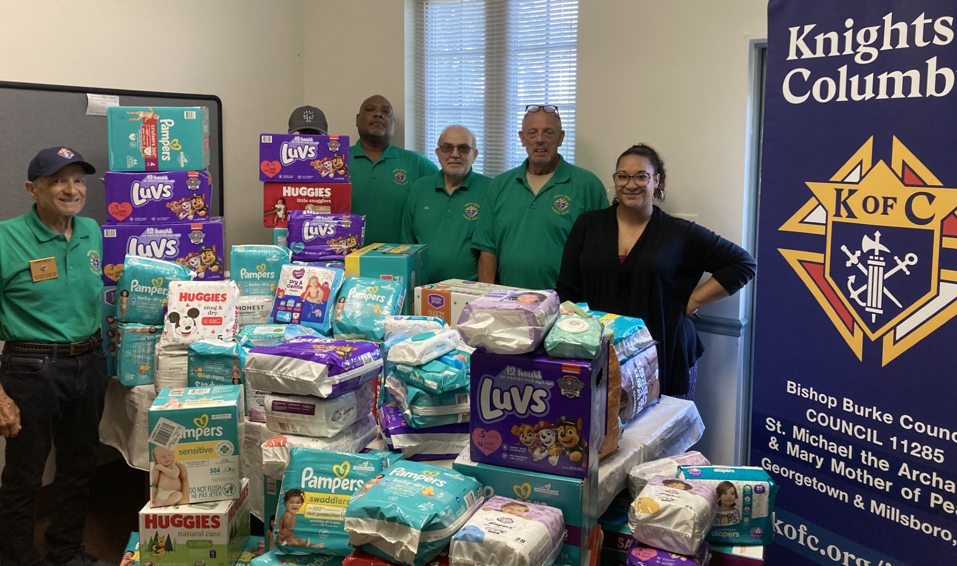 A group of volunteers posing in front of a large donation of pampers for families.