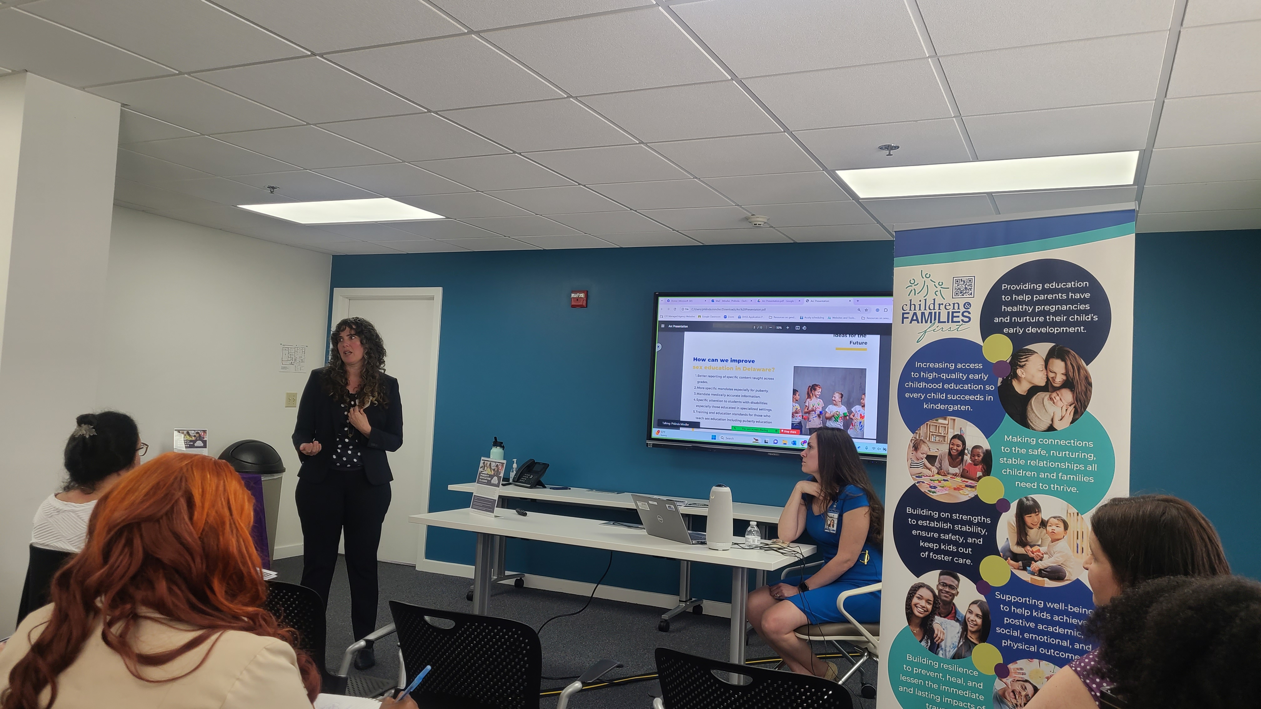 two presenters deliver information to a room of attendees.