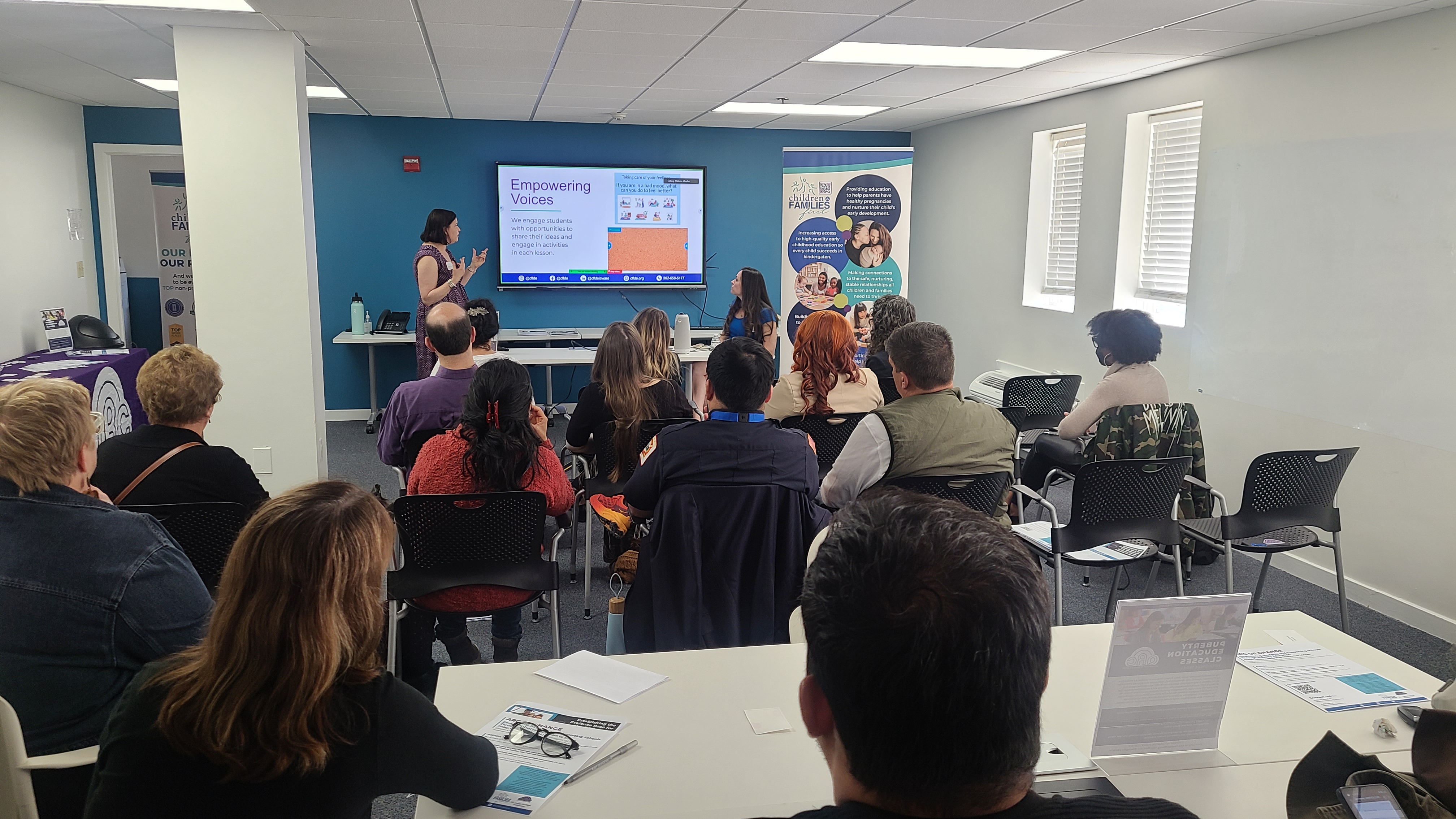 two presenters deliver information to a room of attendees. A title slide reads "Empowering Voices"