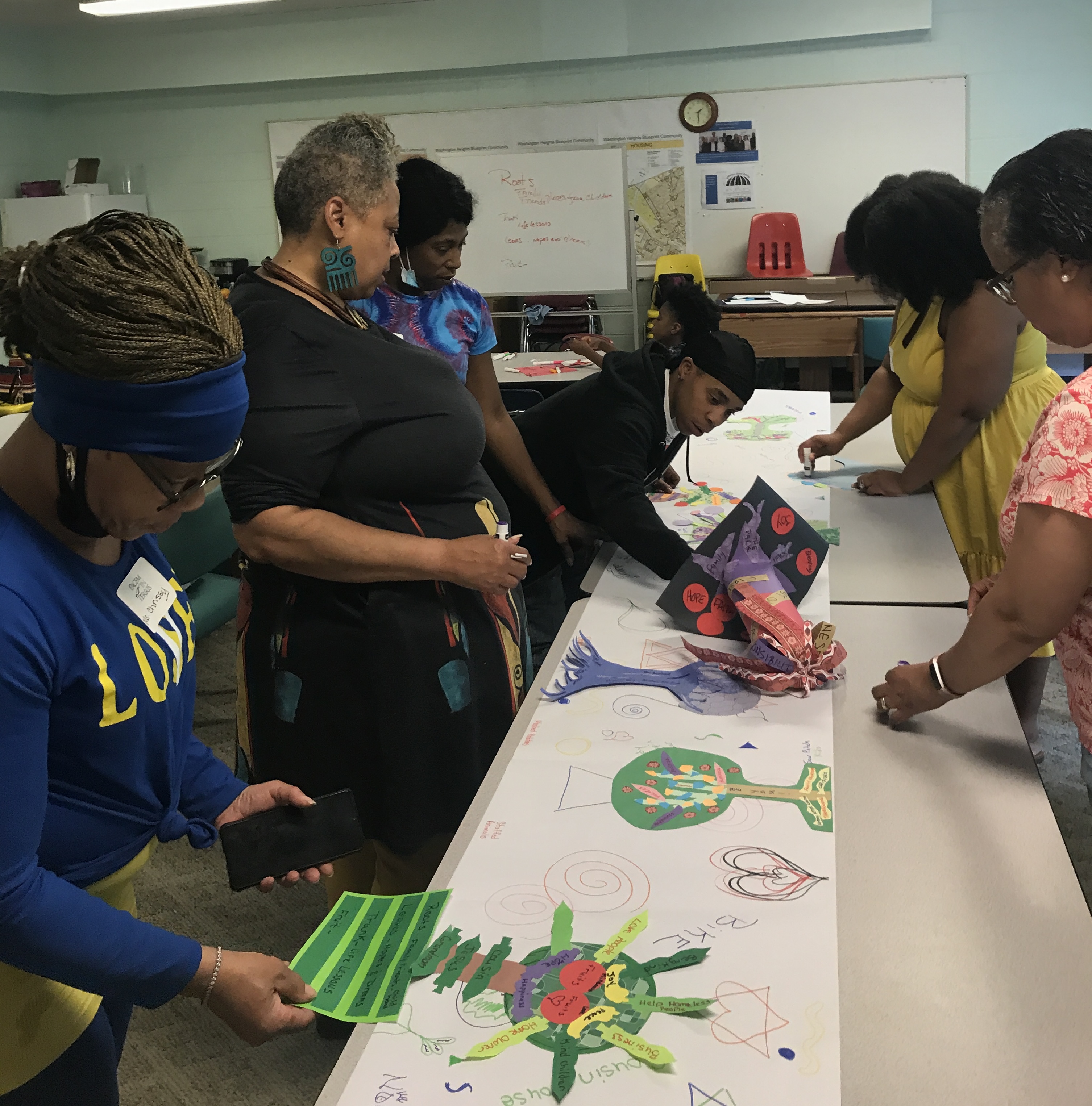 Adult instructors assisting youth on an art project displayed against a long table.