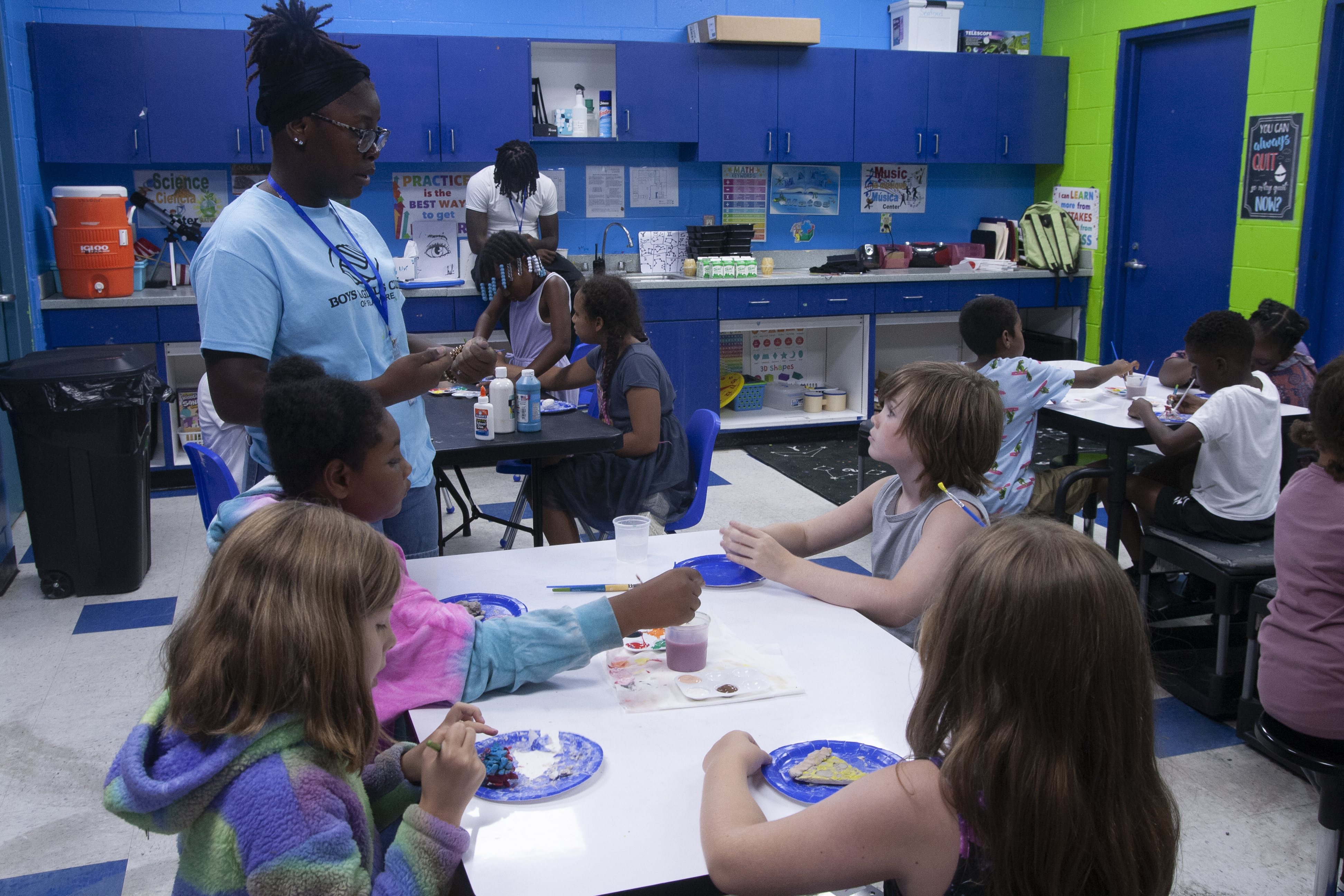 a teen instructor works with elementary school children to make arts and crafts