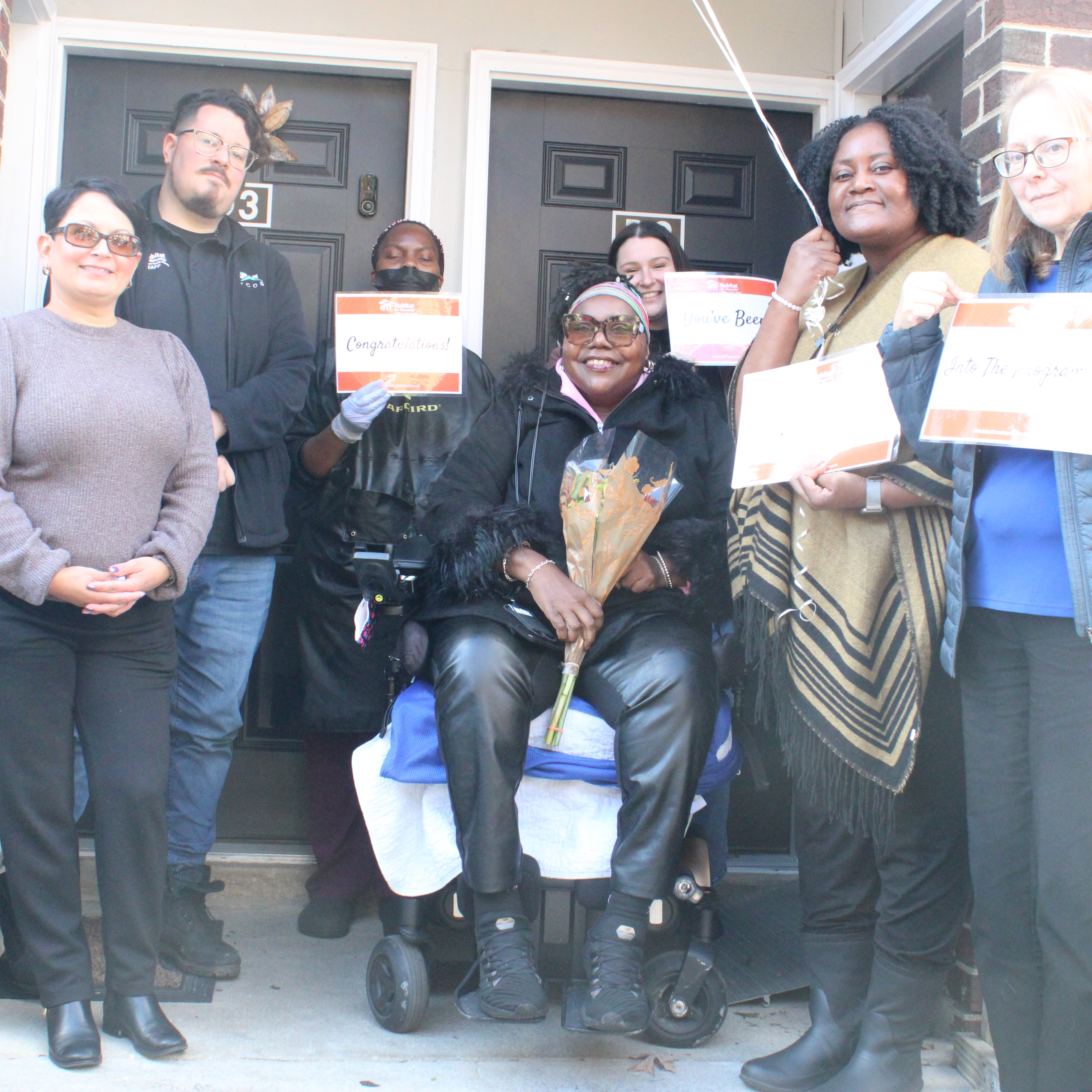 persons standing outside with congratulations signs for a new homeowner.