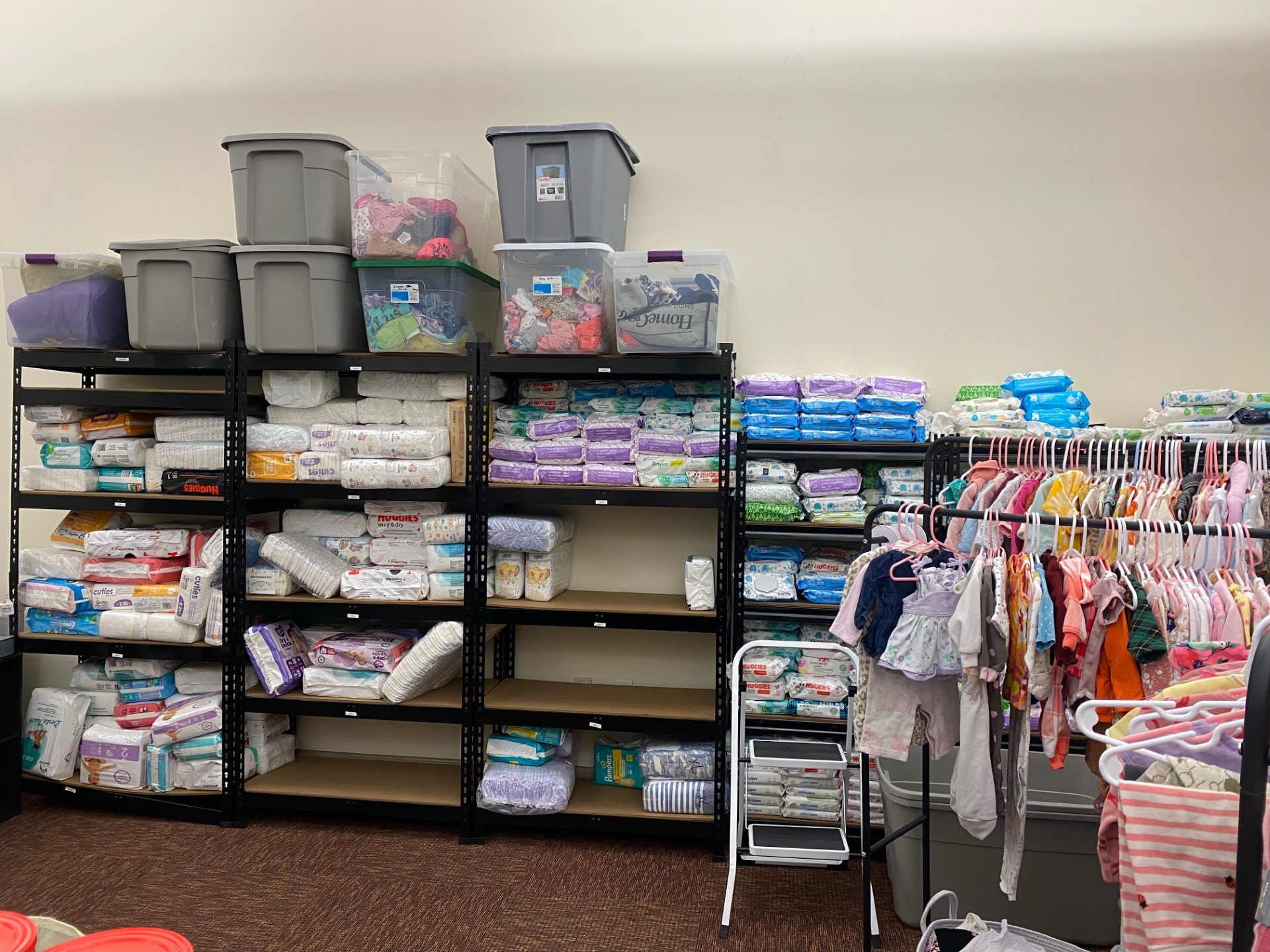 shelves of diapers, baby clothes and other basic need items for parenting individuals in a donation room of a library