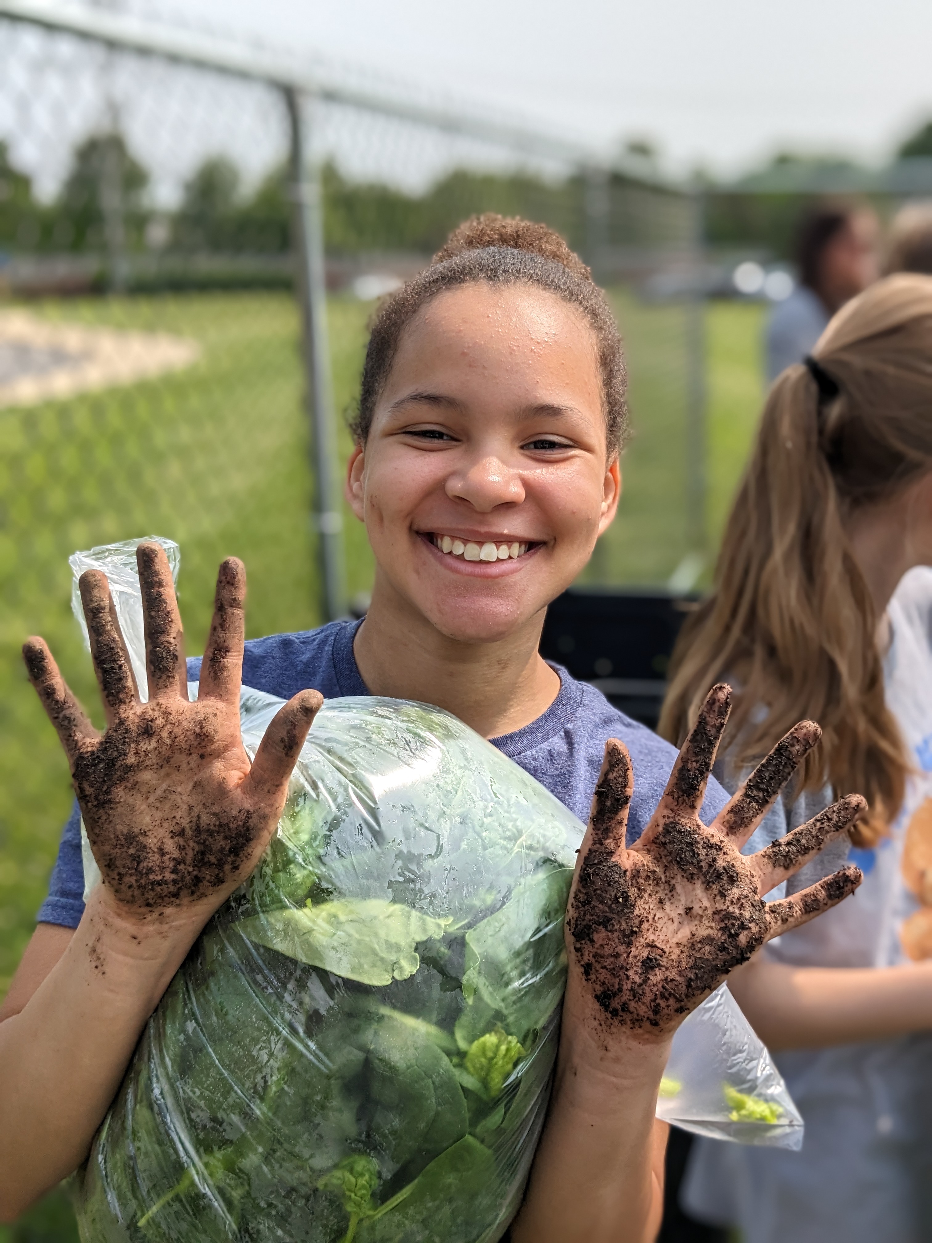 a child holding a bag of vegetables showing their hands covered with dirt to the camera