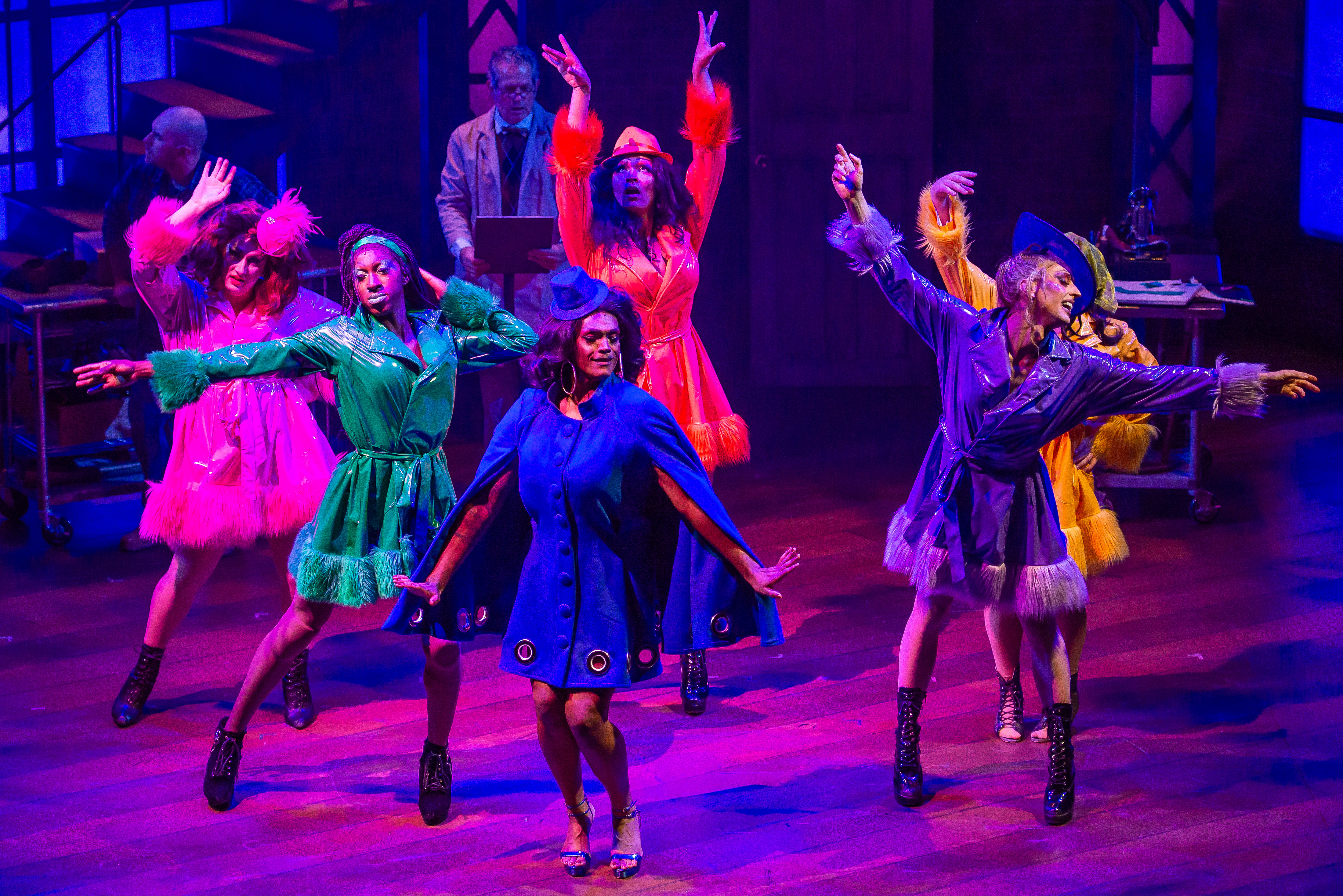 performers on stage dance while lights color the background and stage floor.