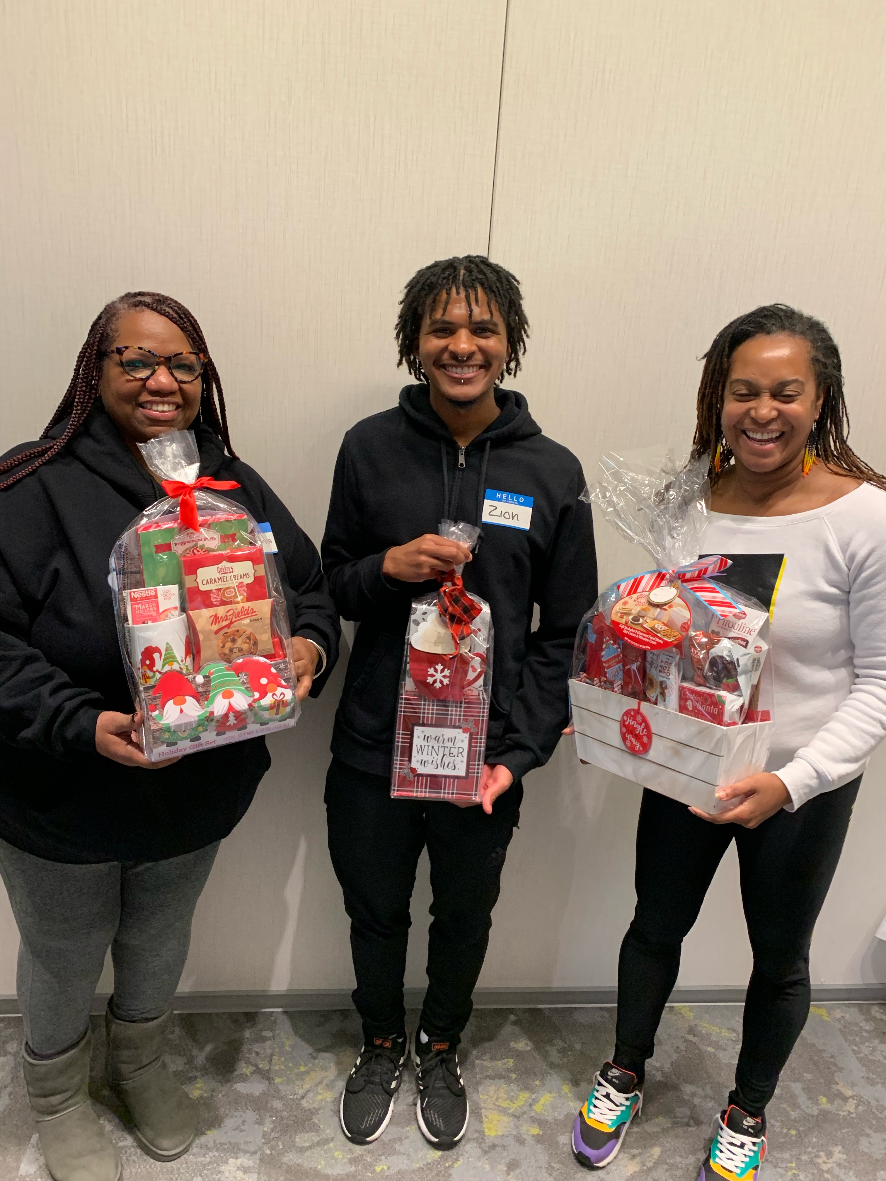 three persons hold care packages containing holiday treats.