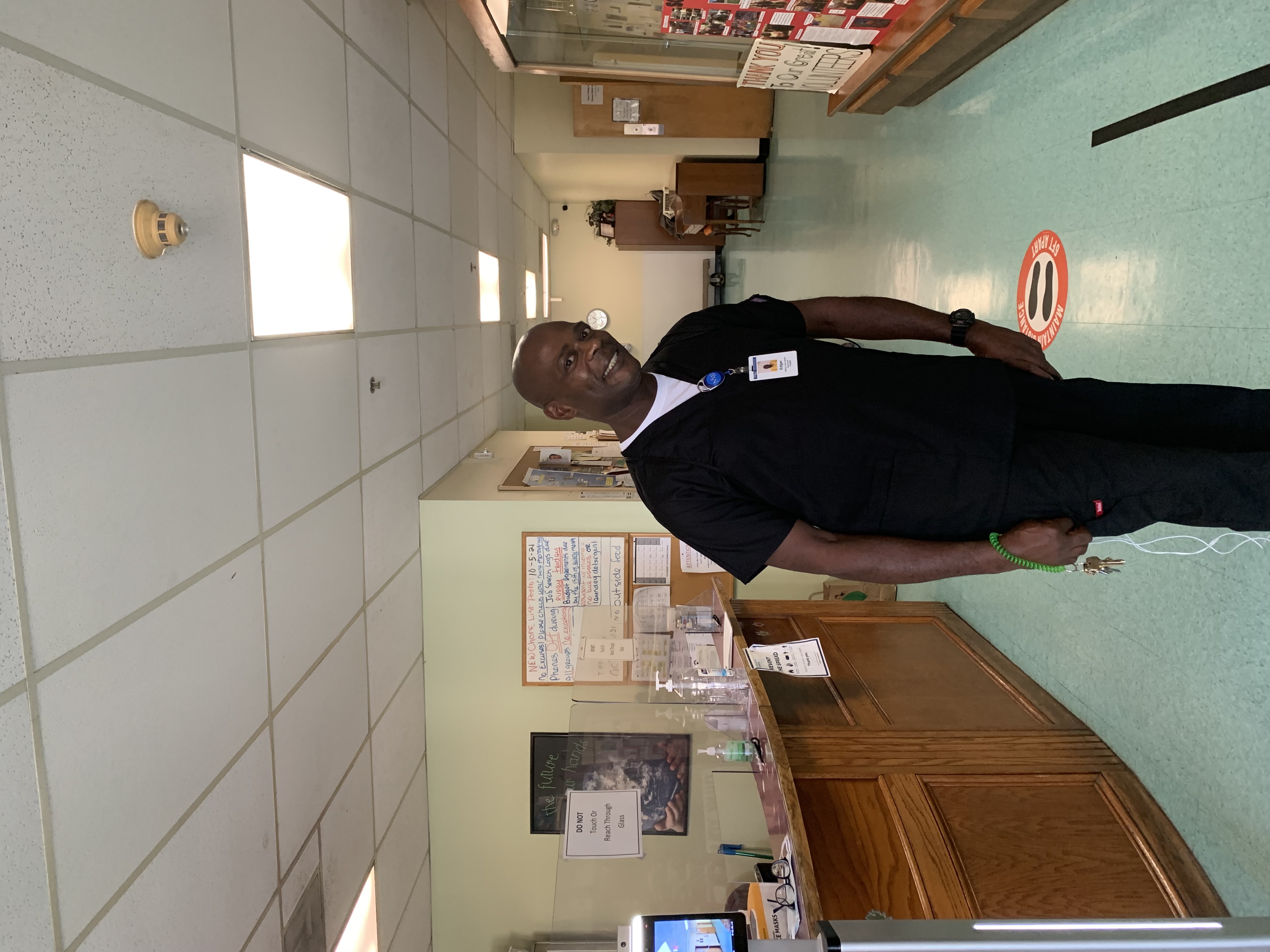 A man posing for the camera while wearing work uniform scrubs within a building hallway.