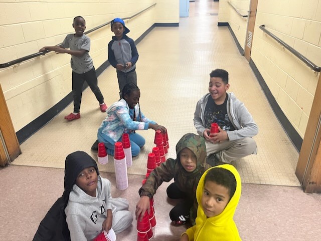 a group of children playing with red cups for an activity in a hallway of a school