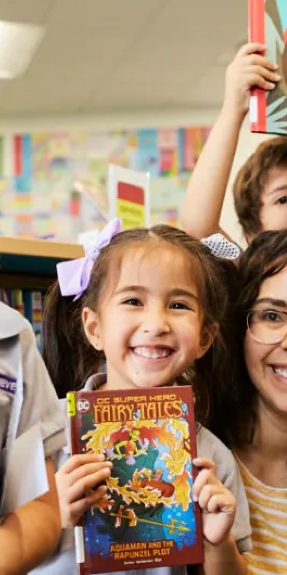 students holding photos of books with their teacher.
