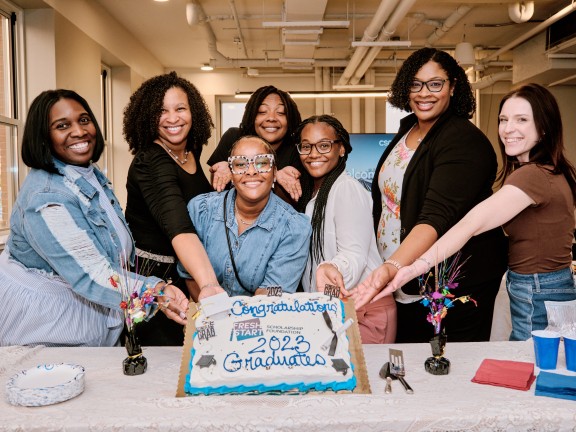 graduates standing in front of a celebratory cake.