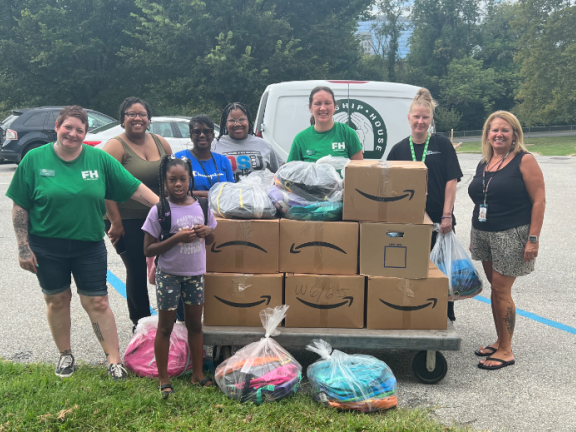 volunteers and staff standing outside a clothing bank behind donations of school uniforms and bookbags. 