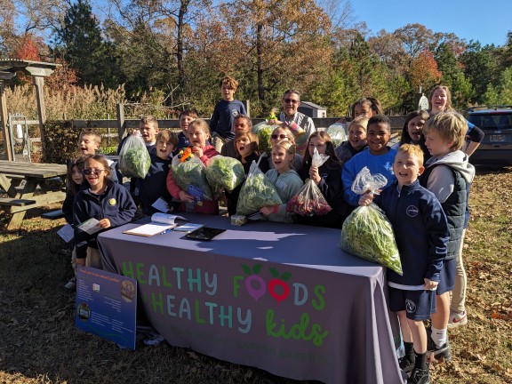 children outdoors with bags of vegetables.