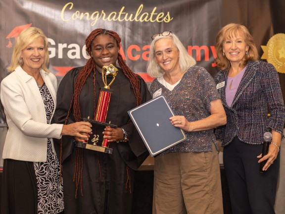 a graduate standing with three adults accepting an award