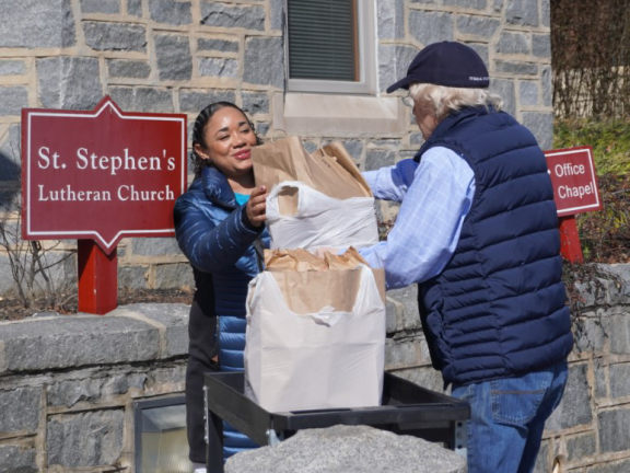 a person handing a distribution of items to another person outside of a lutheran church.