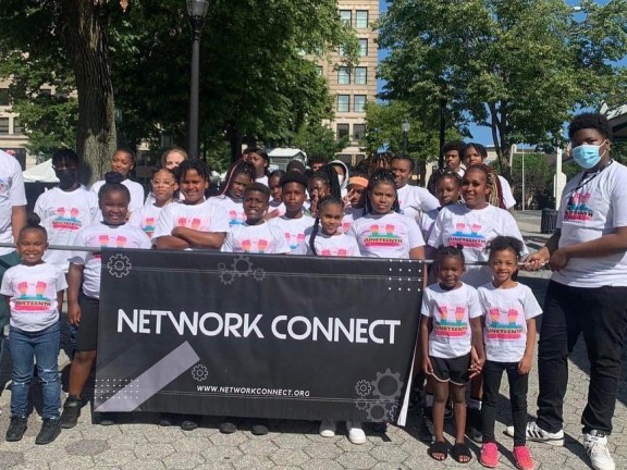 a group of youth and adults standing behind an organizational banner.