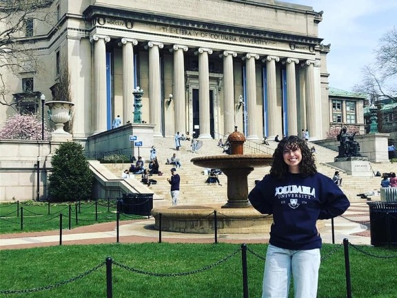 a student standing outside a university with a Columbia university sweatshirt.