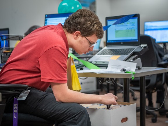 a person in a workspace opening a box at their desk.