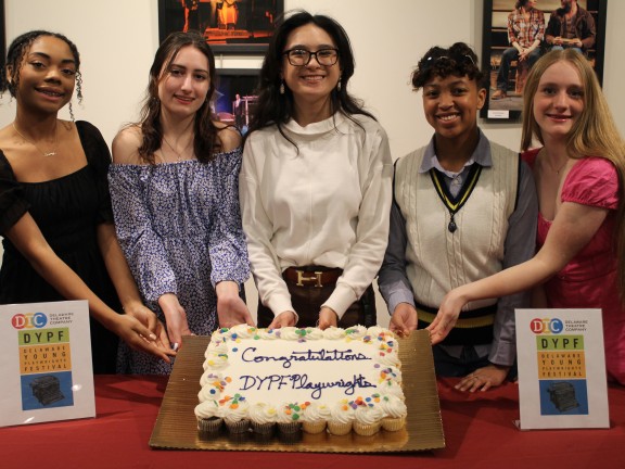 students hold a cake that reads "congratulations" for their participation in a playwright ceremony.