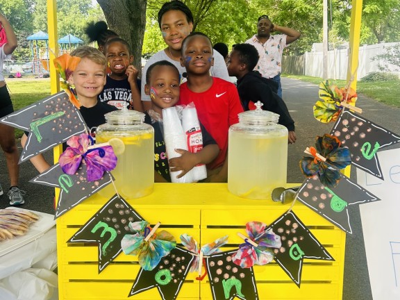 young children standing in front of a lemonade stand.