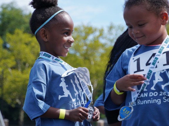 Two children hold medals after participating in a running race.
