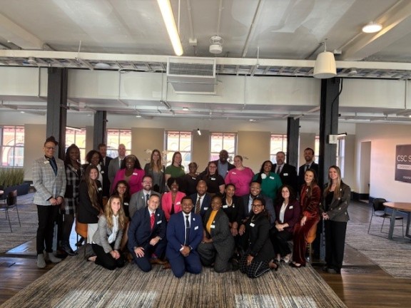 a group of people stand and kneel in a corporate office room to pose for a photo.