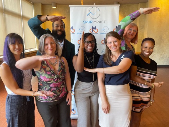 Seven individuals stand to spell the letters 'ELC' for Emerging Leaders Cohort while smiling