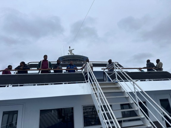 Individuals stand at the edge of a boat's balcony to pose for a camera.