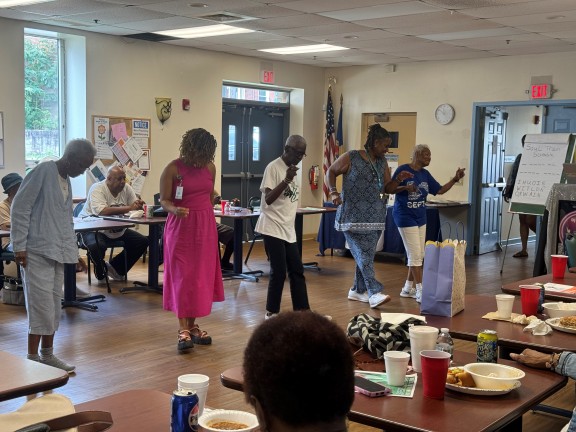 Individuals participating in a line dance while at the Senior Center's recreation and dining room.