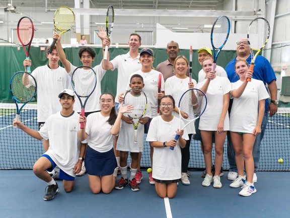 tennis participants posing on the court with their instructors.
