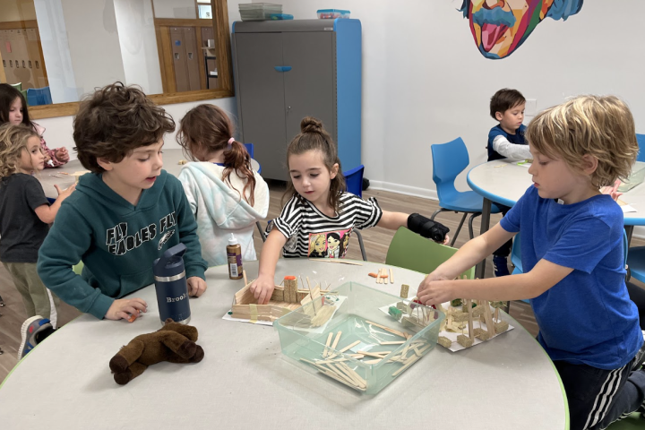 students sit at a classroom table making arts and craft designs.