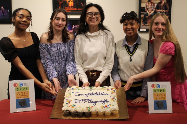 students hold a cake that reads "congratulations" for their participation in a playwright ceremony.