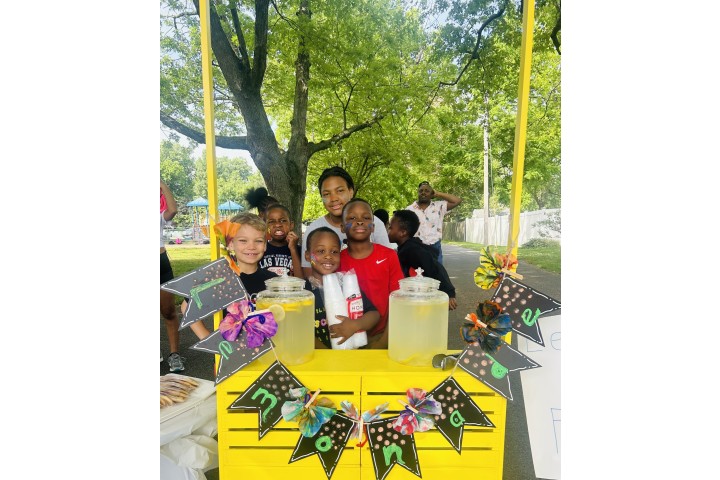 young children standing in front of a lemonade stand.