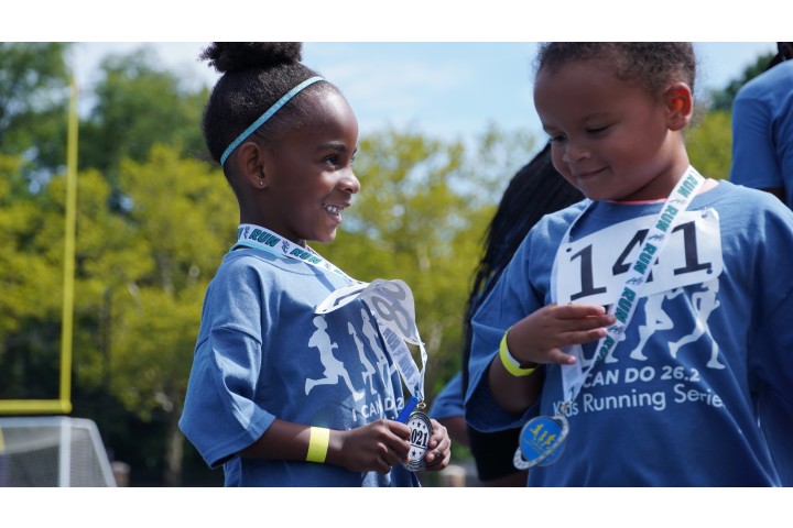 Two children hold medals after participating in a running race.