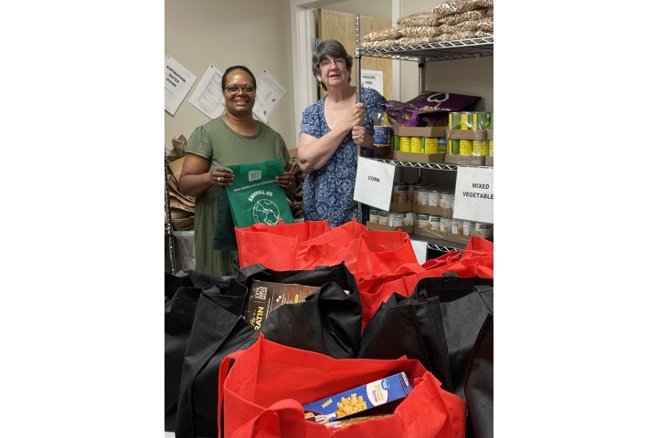 two volunteers stand in a food pantry room with recently donated supplies