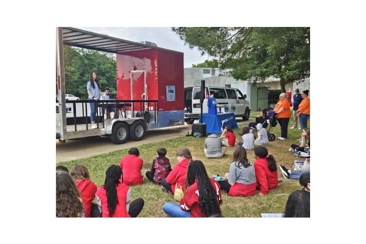 students sit while listening to a play in an outdoor open field.