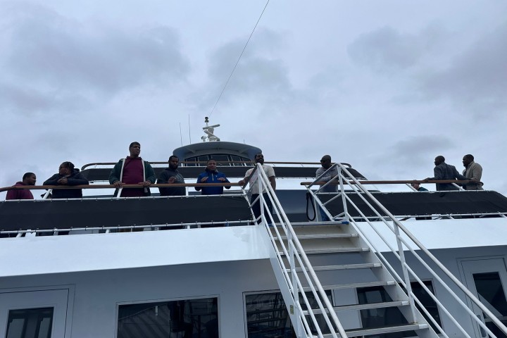 Individuals stand at the edge of a boat's balcony to pose for a camera.