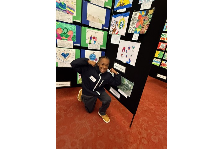 a child posing in front of their art exhibition.
