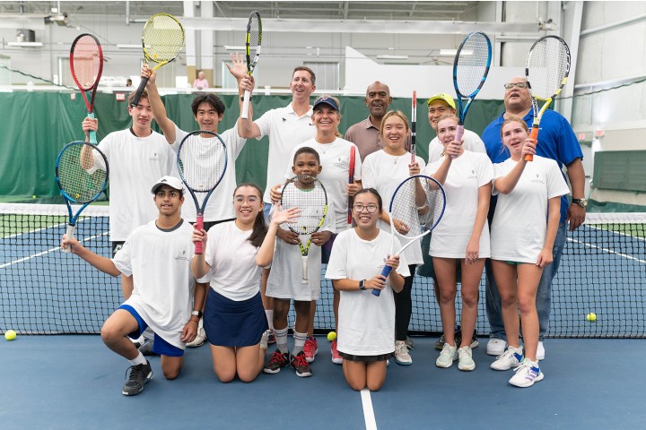 tennis participants posing on the court with their instructors.